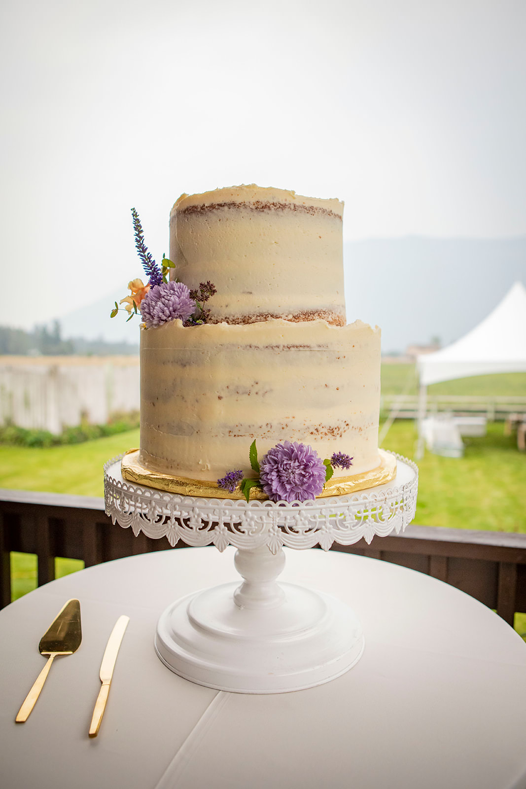 White wedding cake on white cake stand. Gold cake knife set.