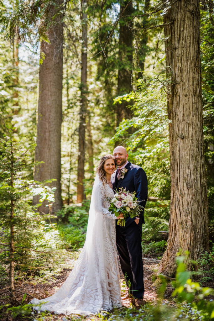 Bride and groom smiling among forest trees at Glacier National Park