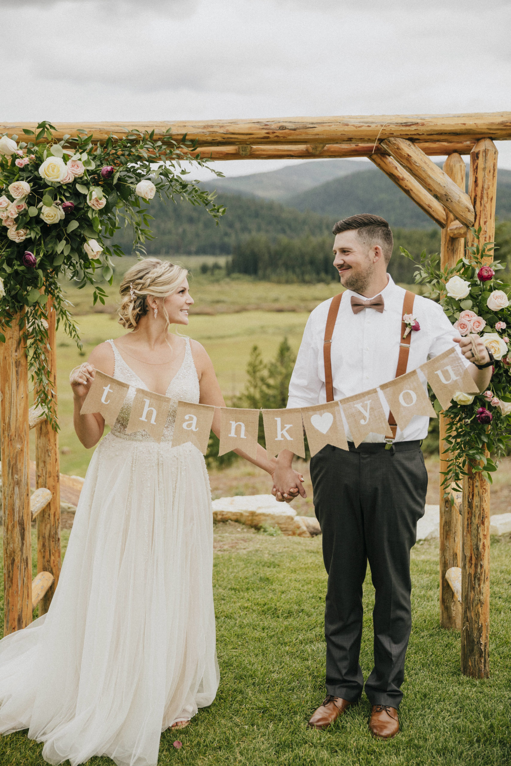 Bride and groom under ceremony arch holding thank you sign at their ranch wedding